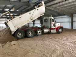 a photo of a dump truck inside of a horse arena dumping washed concrete sand